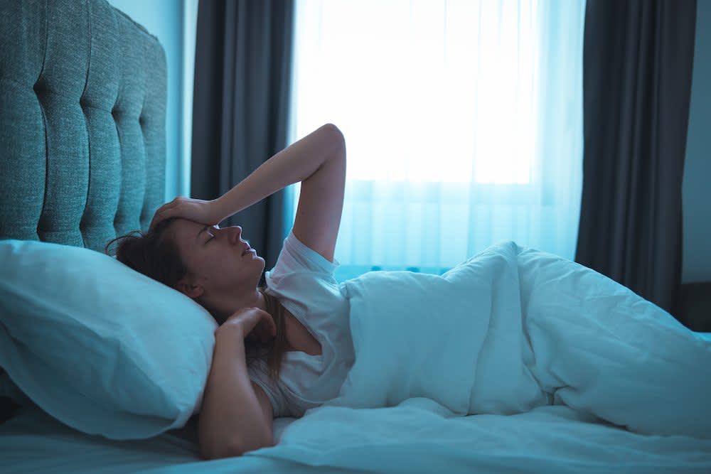 A stock photo of a young woman lying in bed at night, wide awake