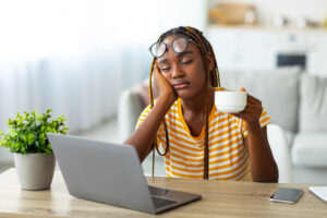 Exhausted woman sitting in front of a laptop with a cup of coffee in her hand