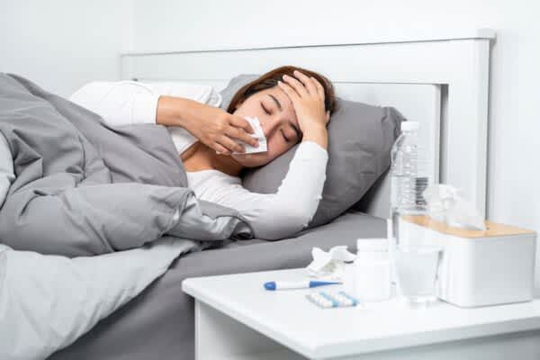 stock photo of a sick woman blowing her nose while lying in bed