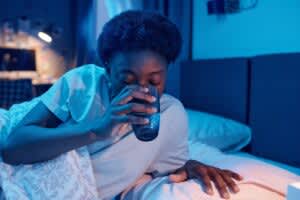 A woman drinks a cup of water in bed