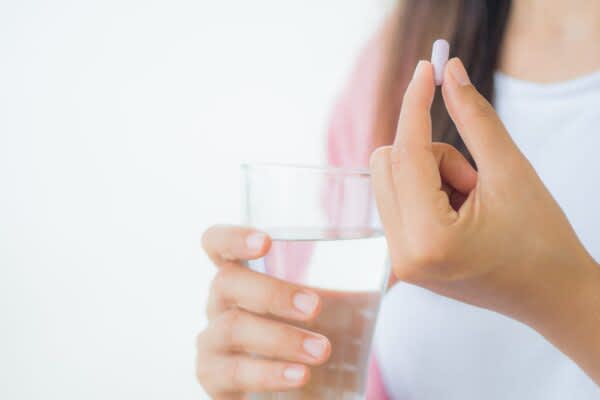 stock photo of a woman holding a pill and a glass of water