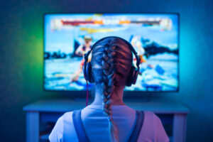 A girl with headphones on plays a video game on a brightly-colored screen