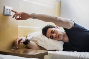 tired man in bed reaching to turn off light