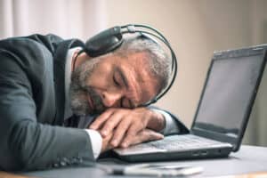 A businessman takes a nap on his laptop with headphones on