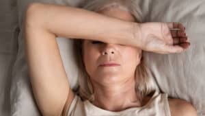 Close up top view of a middle aged woman resting in bed with her arm over her eyes