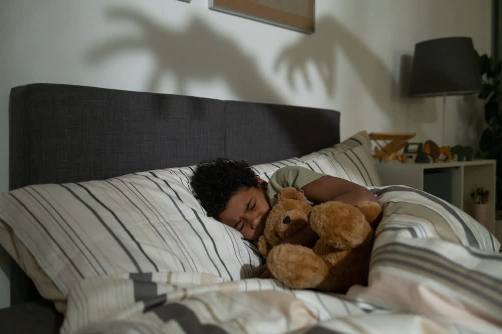 A scared child embraces a teddy bear in bed with a monstrous shadow on the wall