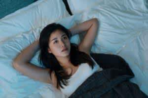 stock photo of a young woman awake in bed with her hands resting behind her head