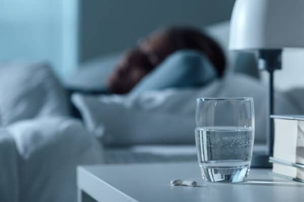 Woman asleep in bed with a glass of water and a sleep aid on the night stand.