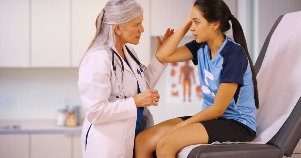 An injured soccer player sits in a doctor's office while holding her head