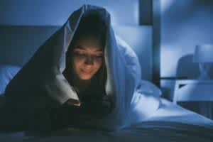 stock photo of a woman using her smartphone in bed at night