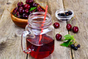 a picture of a glass of cherry juice in a cup with a straw in it and a bowl of cherries placed behind it