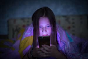 A teen looking at a phone screen in bed