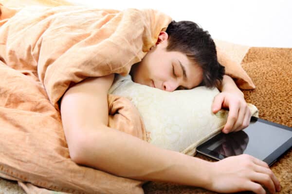 Tired teenager sleeping on the bed with tablet computer