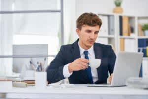 Tired young businessman drinking coffee at his desk during the afternoon slump.