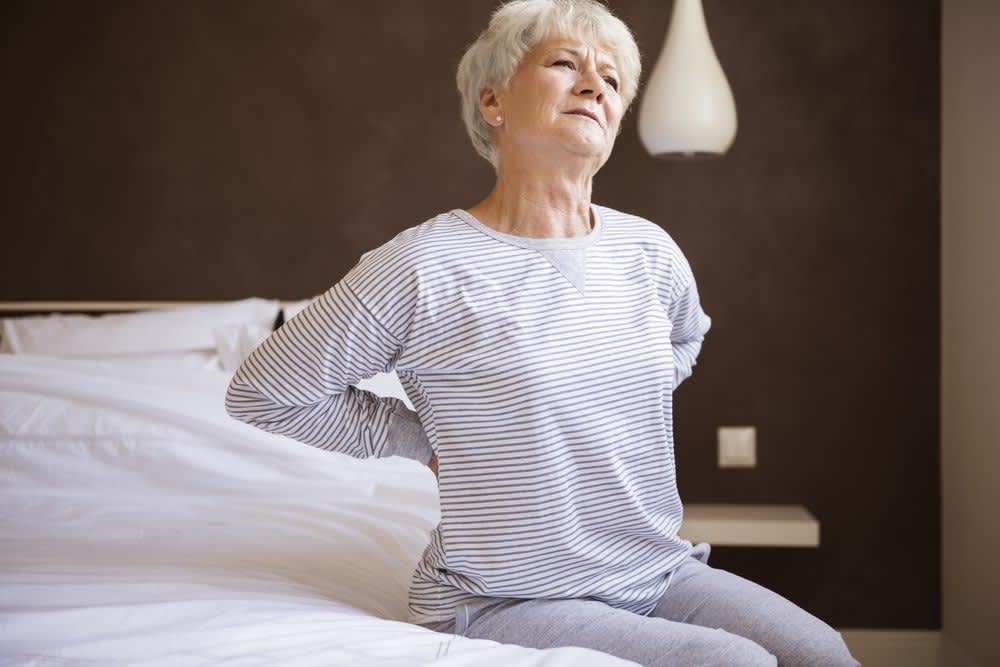 stock photo of a senior woman holding her back in discomfort