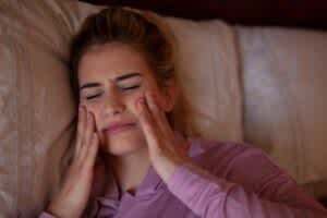 stock photo of a woman lying in bed rubbing her jaw