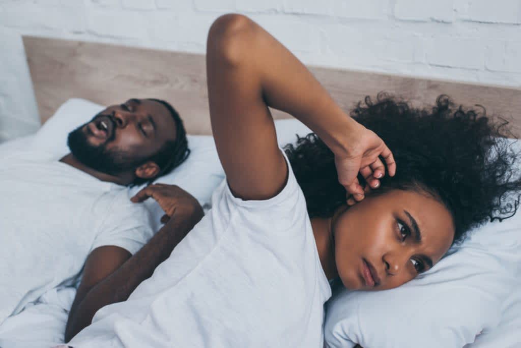 Woman plugging her ears in-bed next to her snoring partner.