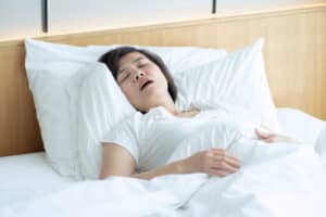 A snoring woman sleeps while propped up on several pillows