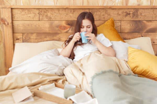 Young woman relaxing in bed with a cup of tea.